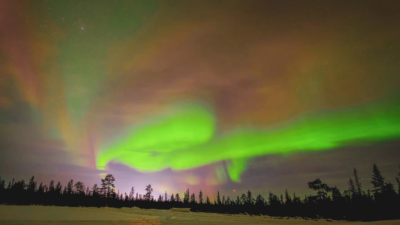 The Northern Lights against a starry sky, illuminating snow-covered landscapes in Swedish Lapland.