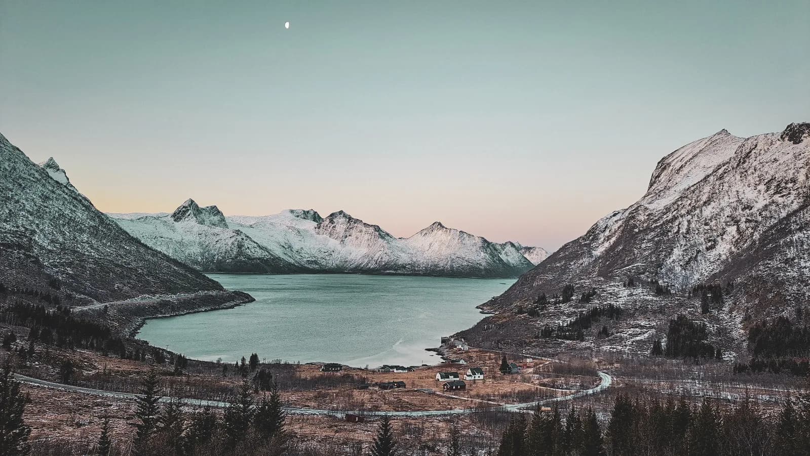 Een panoramisch uitzicht op de fjorden van Senja, bergen met besneeuwde toppen en een vredig meer bij zonsondergang.