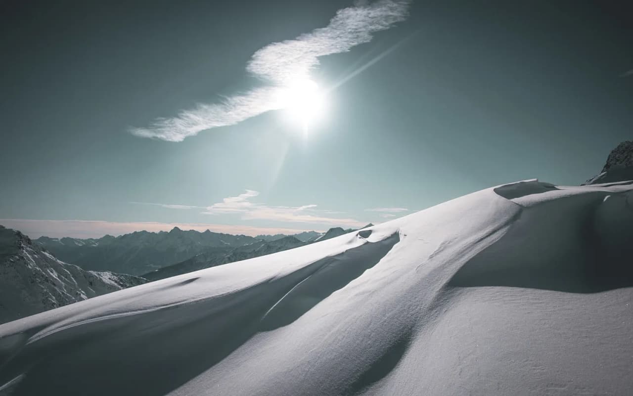 Vastes étendues de neige sous un soleil éclatant, montagnes majestueuses à l'horizon.
