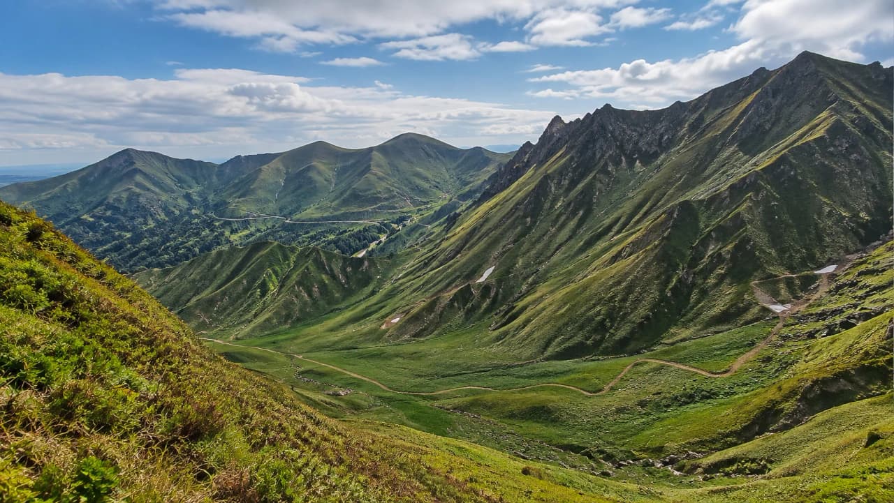 Vastes montagnes verdoyantes sous un ciel bleu, invitant à l'aventure et à la randonnée.