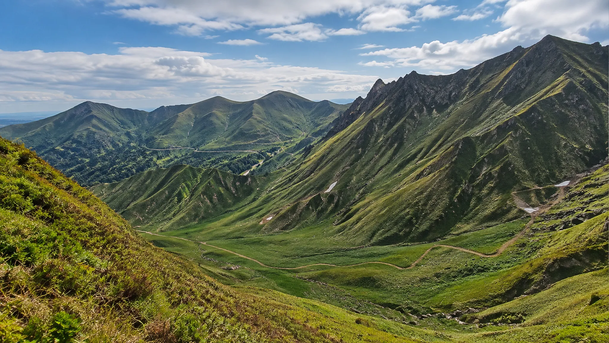 Vastes montagnes verdoyantes sous un ciel bleu, invitant à l'aventure et à la randonnée.
