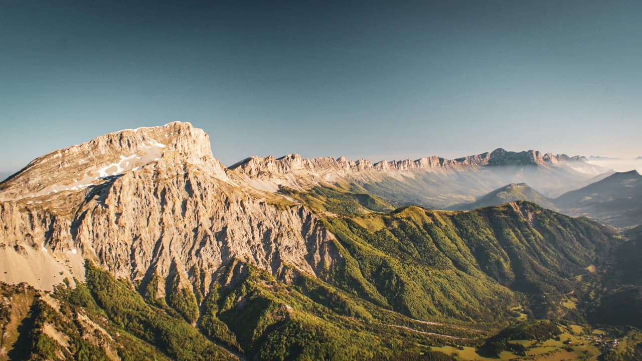Een lachende klimmer past zijn uitrusting aan op de top van de Mont Aiguille, omringd door adembenemende landschappen.