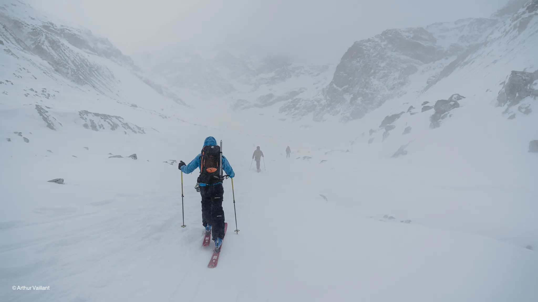 Skiers making their way through an Alpine snowstorm, surrounded by majestic mountains.