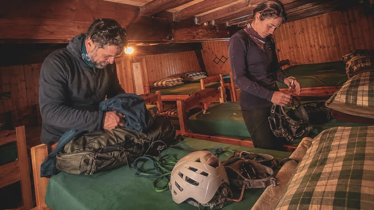 Two mountaineers are preparing their kit for the ascent of the Breithorn in a cosy mountain hut.