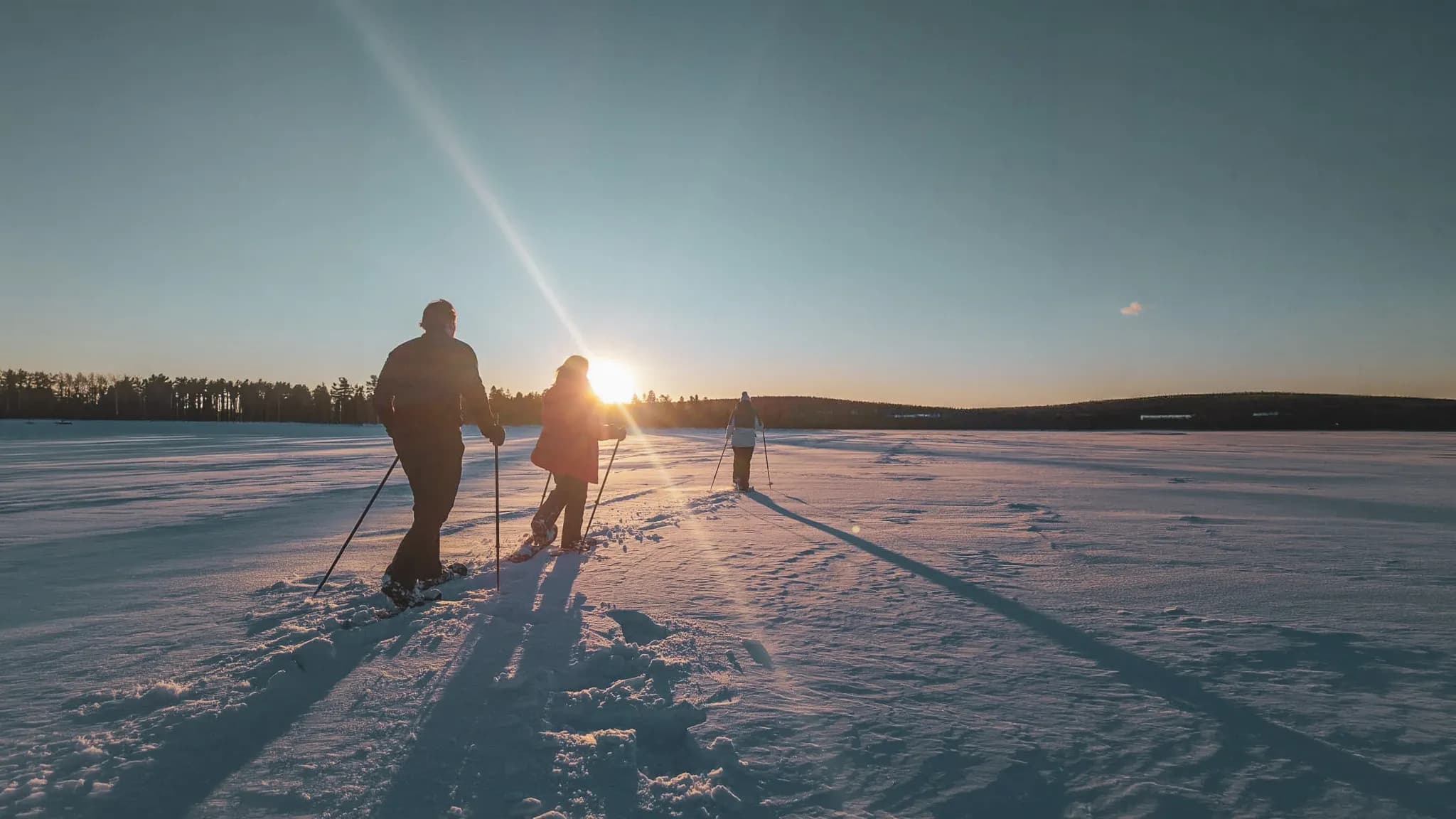 Drie sneeuwschoenwandelaars verkennen een besneeuwd landschap in de stralende zon van Lapland.