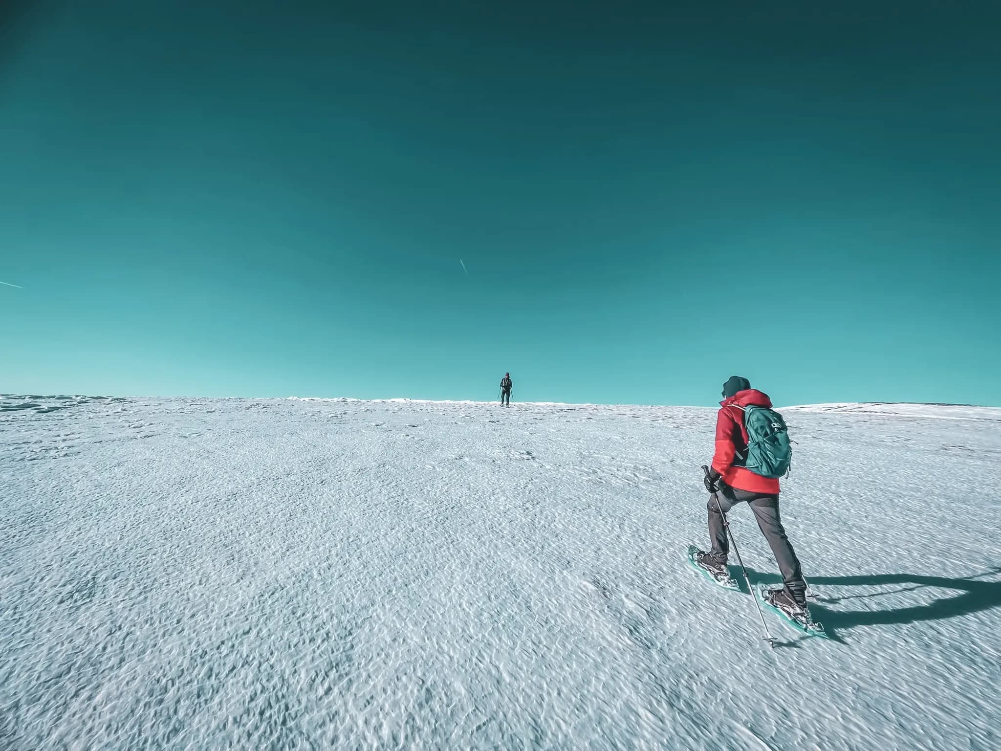 Two hikers on snowshoes on immaculate snow under a turquoise sky, ready to explore the Vosges.