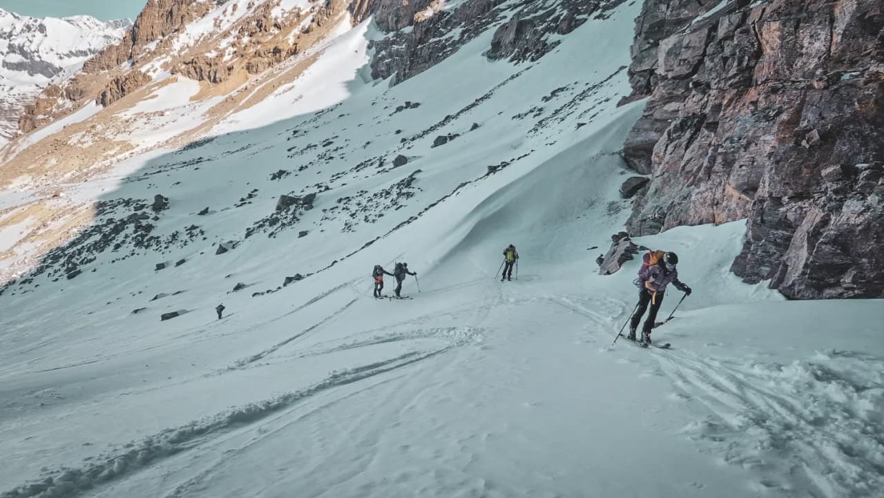 Groupe de skieurs ascendant un sentier enneigé, entouré de majestueuses montagnes alpines.