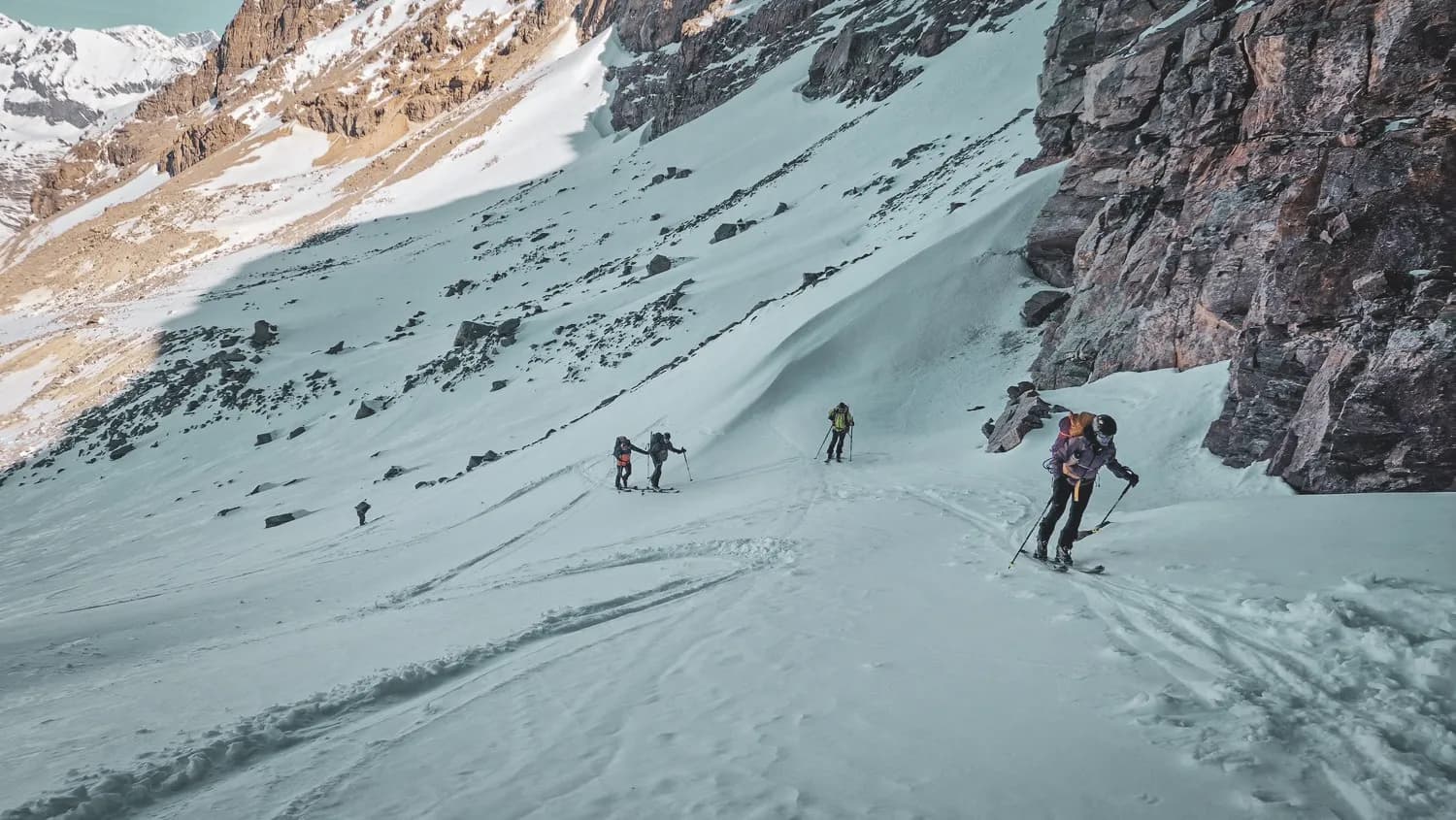 Groupe de skieurs ascendant un sentier enneigé, entouré de majestueuses montagnes alpines.
