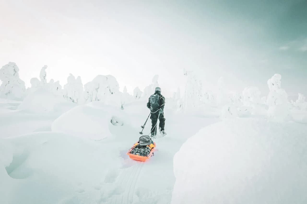 Homme traçant son chemin dans la neige immaculée de Laponie, tirant une luge colorée.