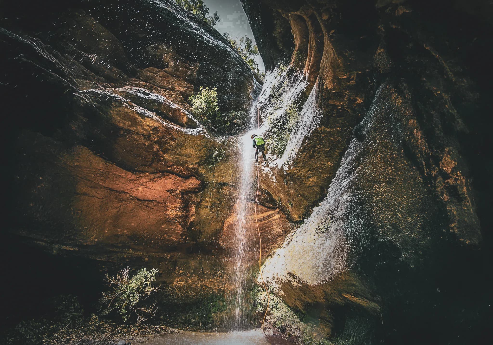 An adventurer descending a majestic gorge, with a dazzling waterfall in the background.