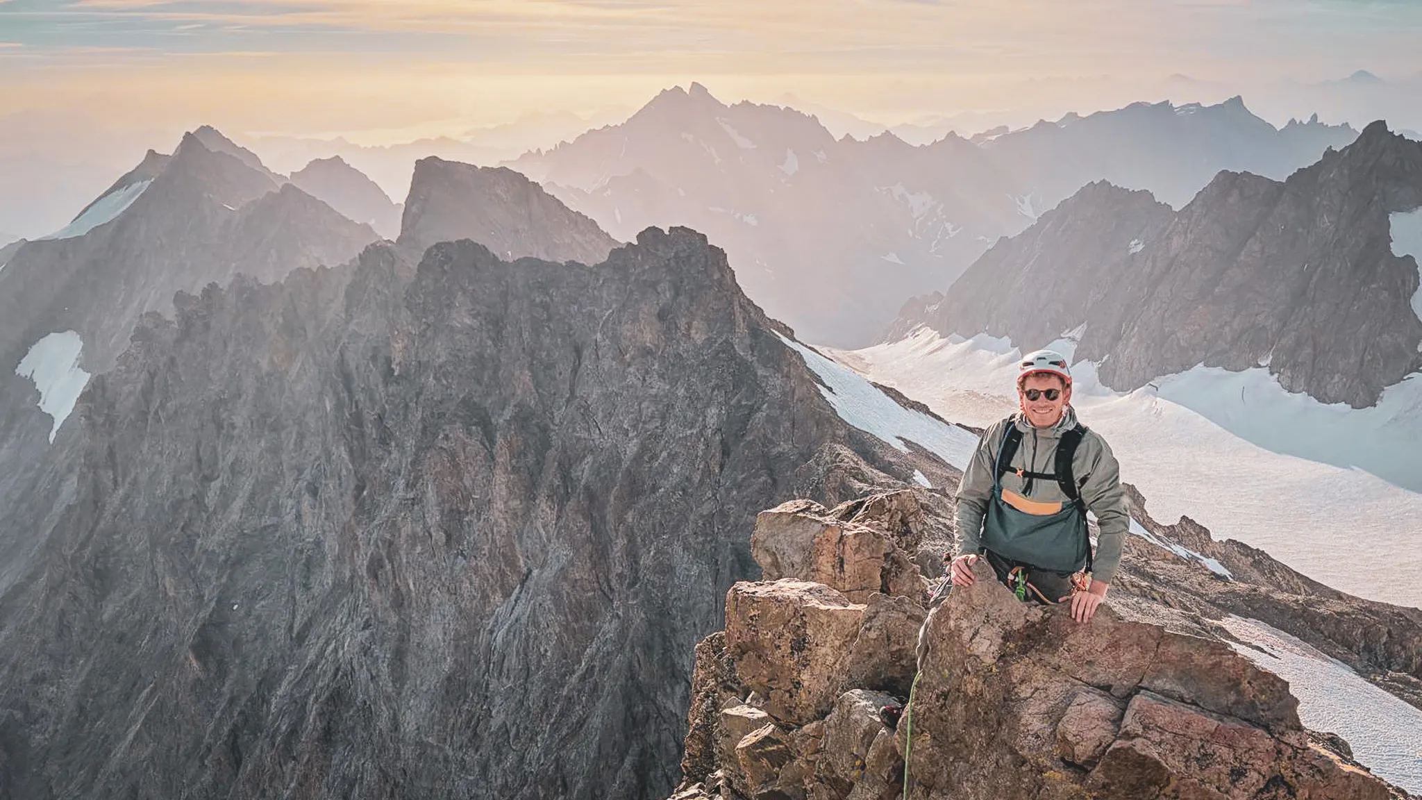 Alpiniste souriant au sommet d'une montagne des Écrins, entouré de paysages grandioses.