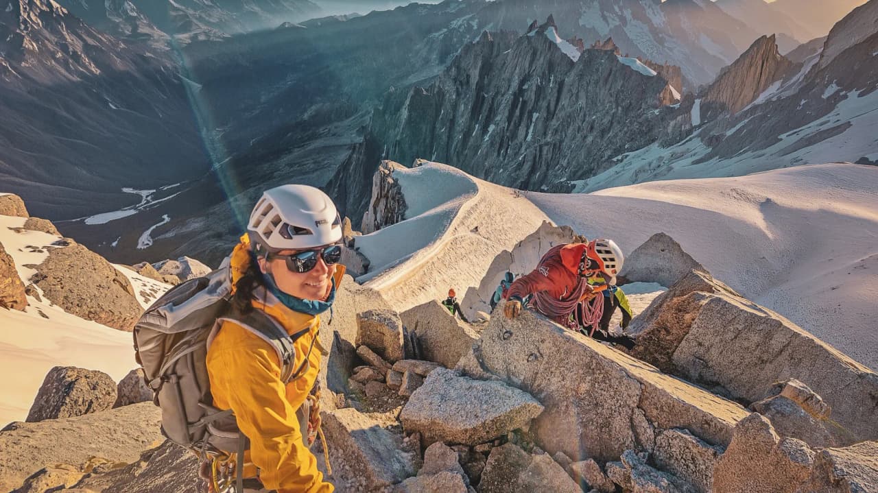 Lachende klimmers op steile rotsen, Alpenvallei en majestueuze bergtoppen op de achtergrond.