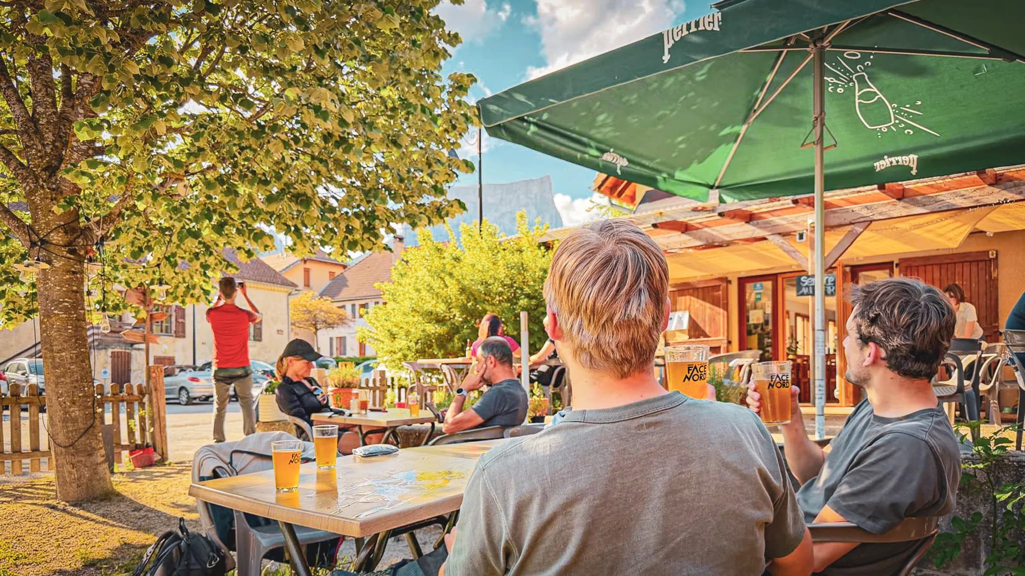 A group of friends relaxing on a terrace with a view of Mont Aiguille, enjoying some refreshing drinks.
