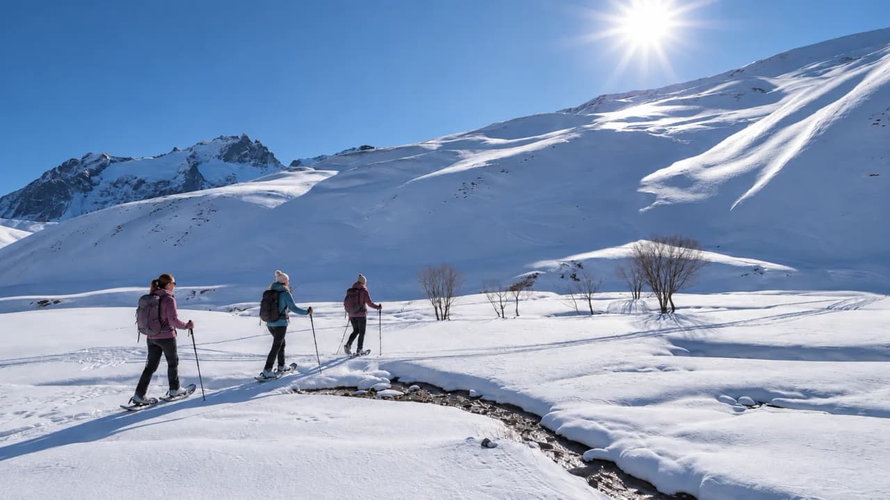 Three women snowshoeing through a snow-covered landscape, beneath a brilliant blue sky.