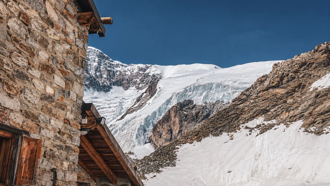 Een stenen Berghut met uitzicht op de majestueuze besneeuwde toppen van de Alpen, die uitnodigt tot een avontuur in de bergen.