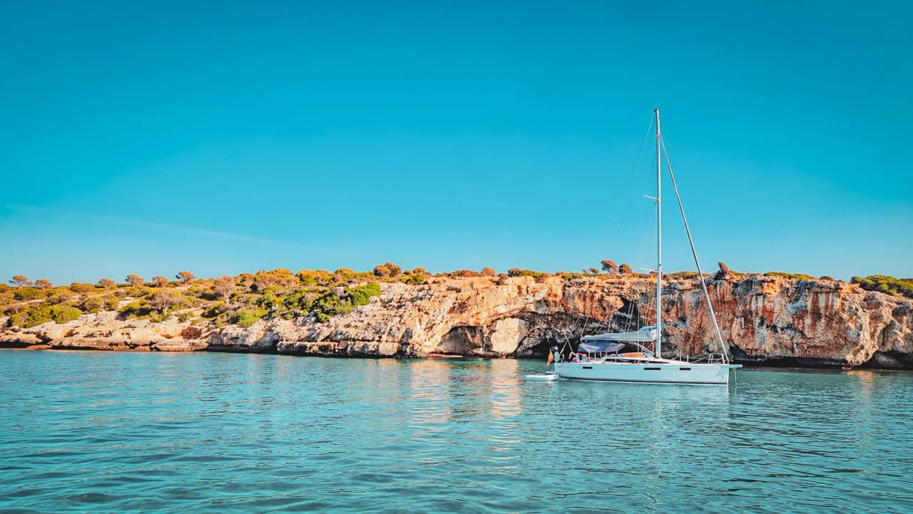 A sailing boat peacefully moored near sunny coves in the Balearic Islands, with a relaxing atmosphere.