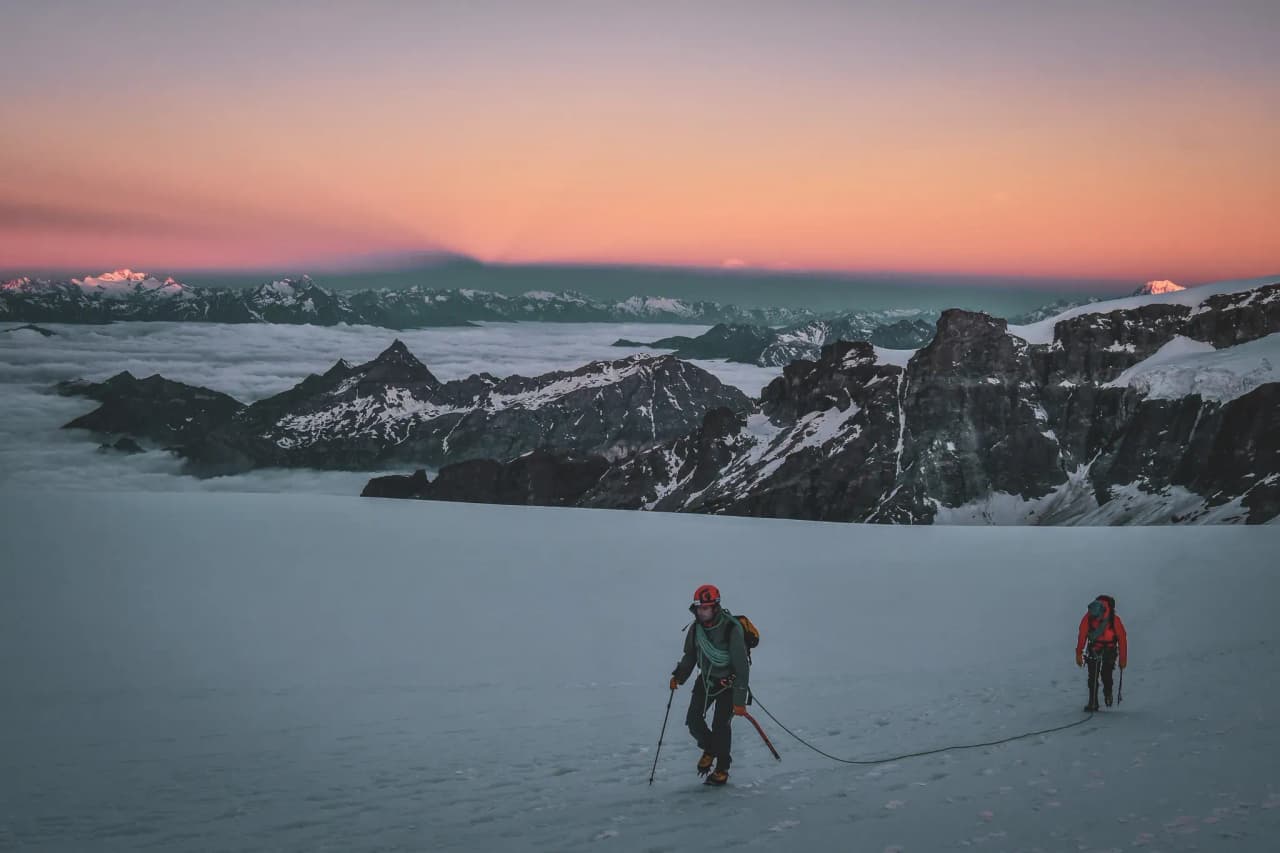 Alpinistes traversant un glacier au petit matin, face à des sommets majestueux.