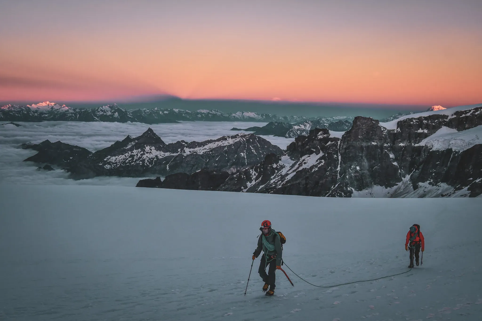 Alpinistes traversant un glacier au petit matin, face à des sommets majestueux.