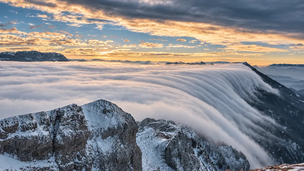 A spectacular view of the snow-capped mountains of the Vercors, shrouded in clouds beneath a colourful sky.