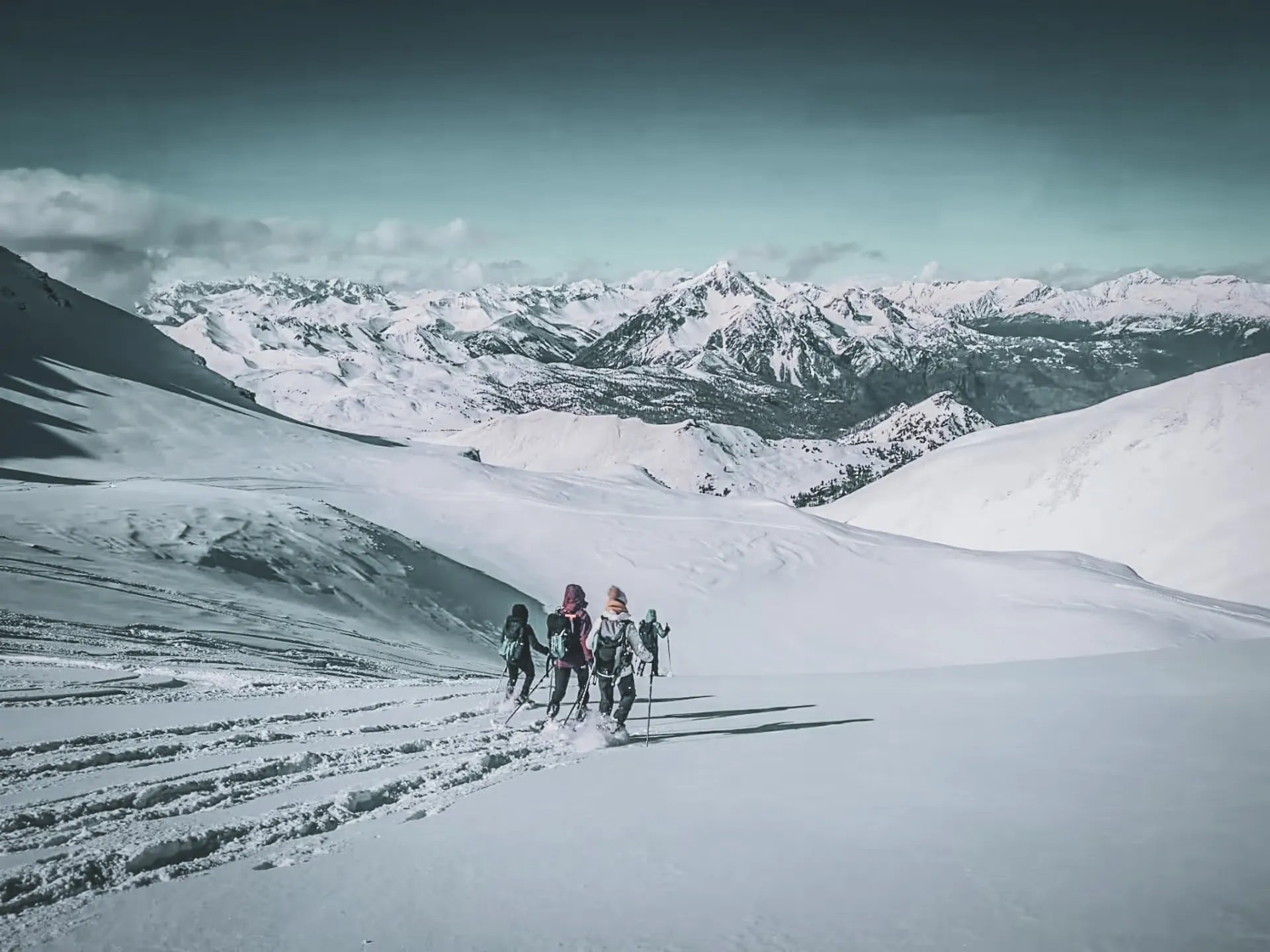A group of hikers venture into a snow-covered Alpine landscape between majestic peaks.