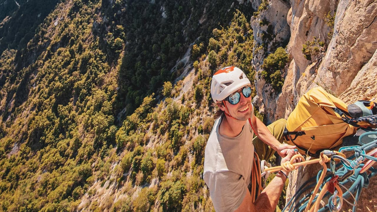 A smiling climber on a sunny cliff in the Gorges du Verdon, surrounded by nature.
