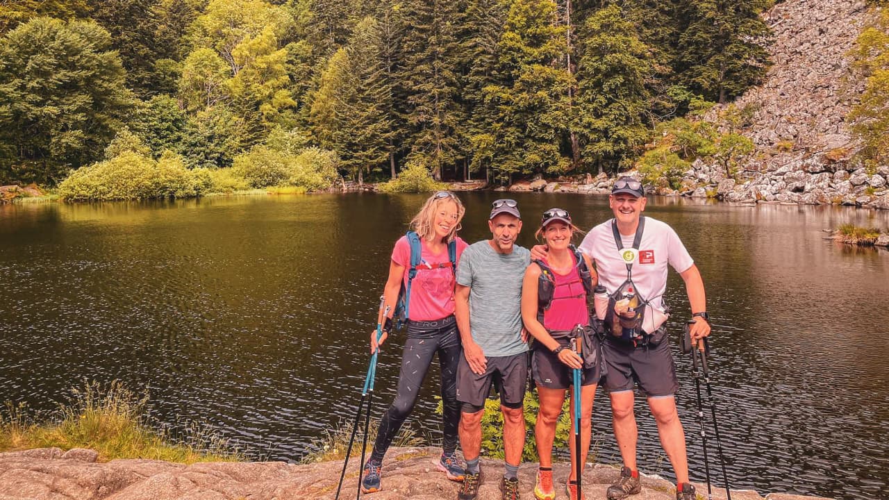 Groupe de randonneurs souriants au bord d'un lac entouré de verdure dans les Vosges.