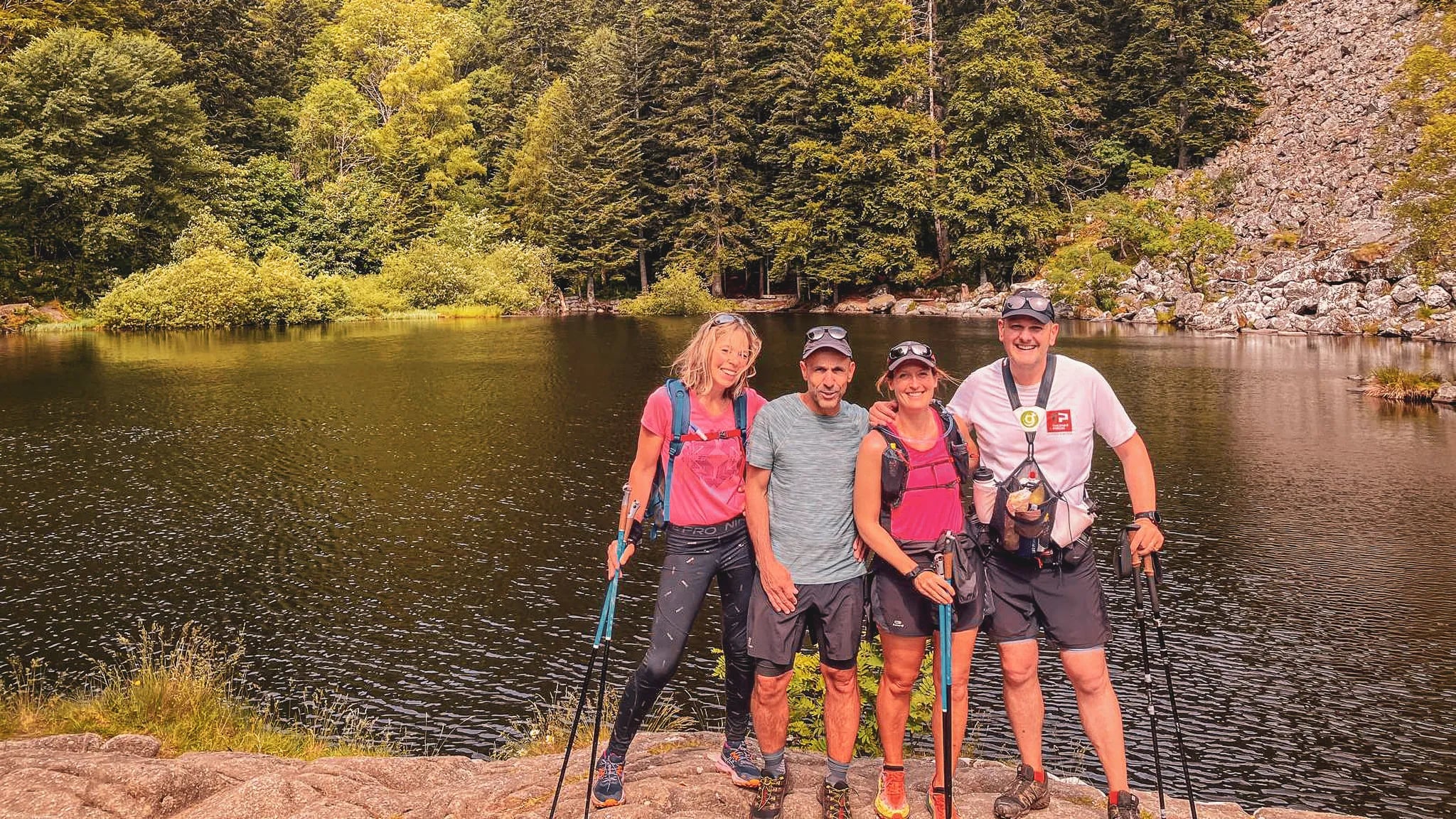 Groupe de randonneurs souriants au bord d'un lac entouré de verdure dans les Vosges.