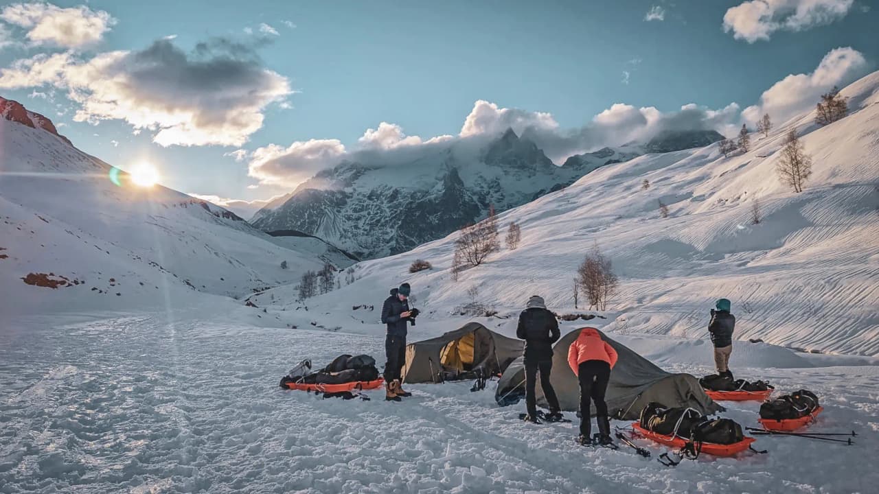 A group camping beneath the snow-capped mountains at sunrise, with a sense of adventure and the great outdoors.