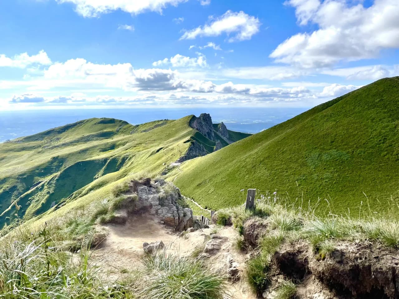 Het groene landschap van het Centraal Massief, kronkelende paden tussen vulkaantoppen en blauwe luchten.
