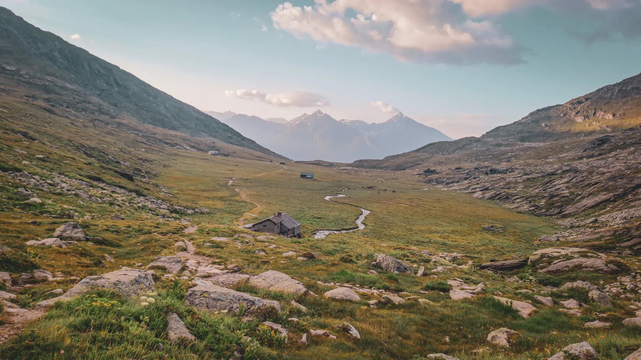 A green valley with a welcoming Mountain hut, surrounded by majestic mountains.