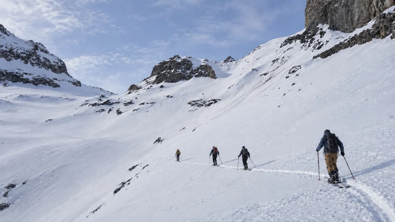 Three walkers are making their way along a snow-covered path, surrounded by majestic mountains.