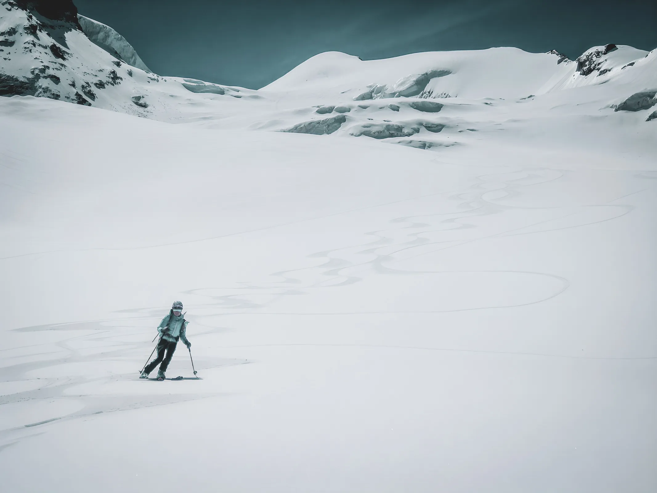 skieur solitaire sur un vaste glacier blanc, devant des sommets majestueux sous le ciel bleu.