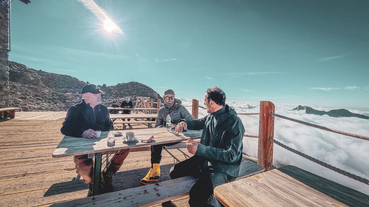 Three mountaineers are enjoying a break in the mountains, surrounded by clouds and majestic peaks.