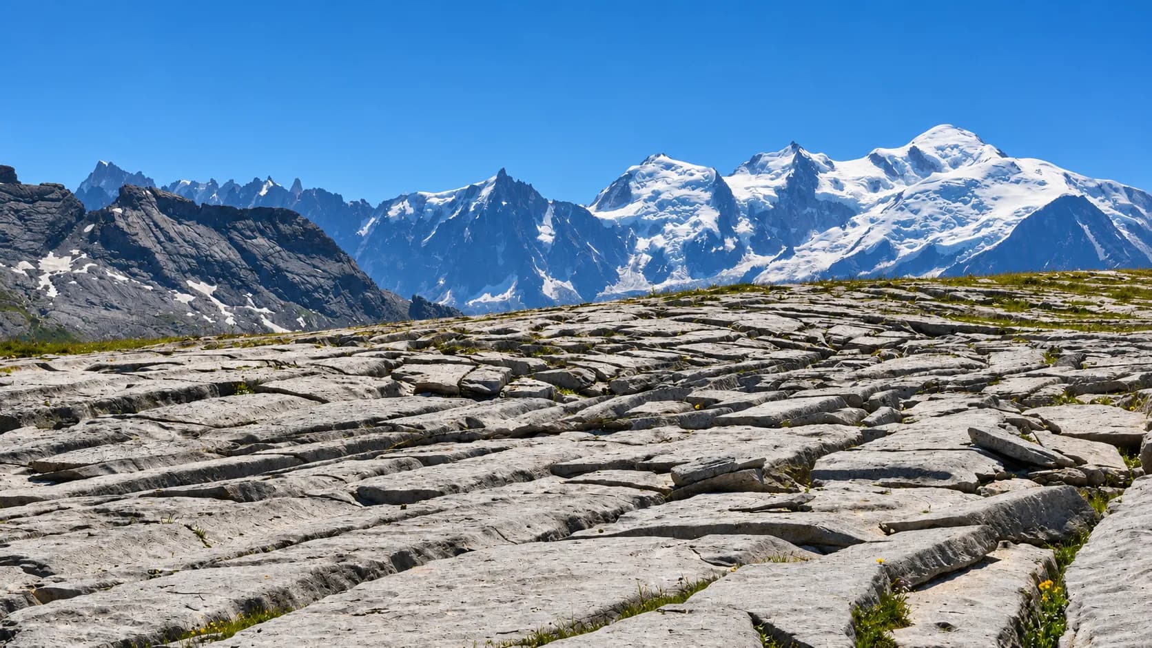 A unique lapiaz, with the snow-capped peaks of the Alps towering above it against a brilliant blue sky.