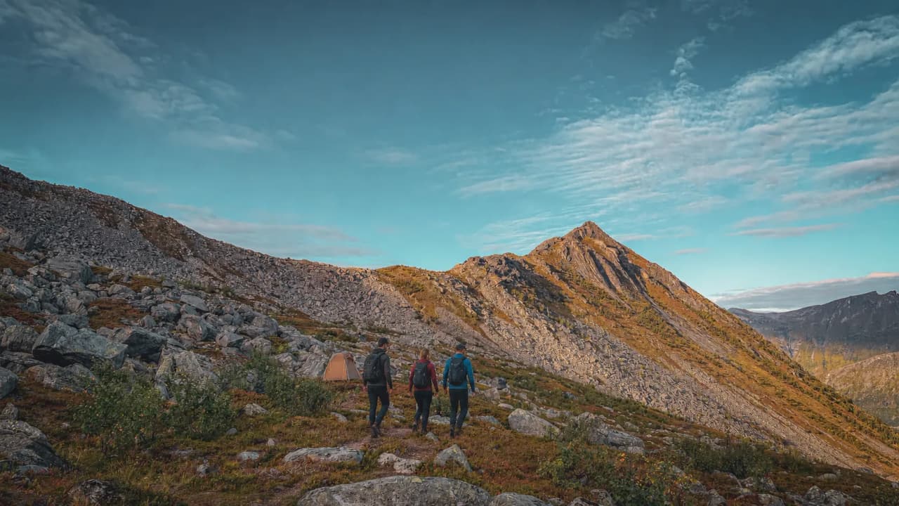 Drie wandelaars banen zich een weg langs een spectaculair pad omringd door bergen en rotsen.