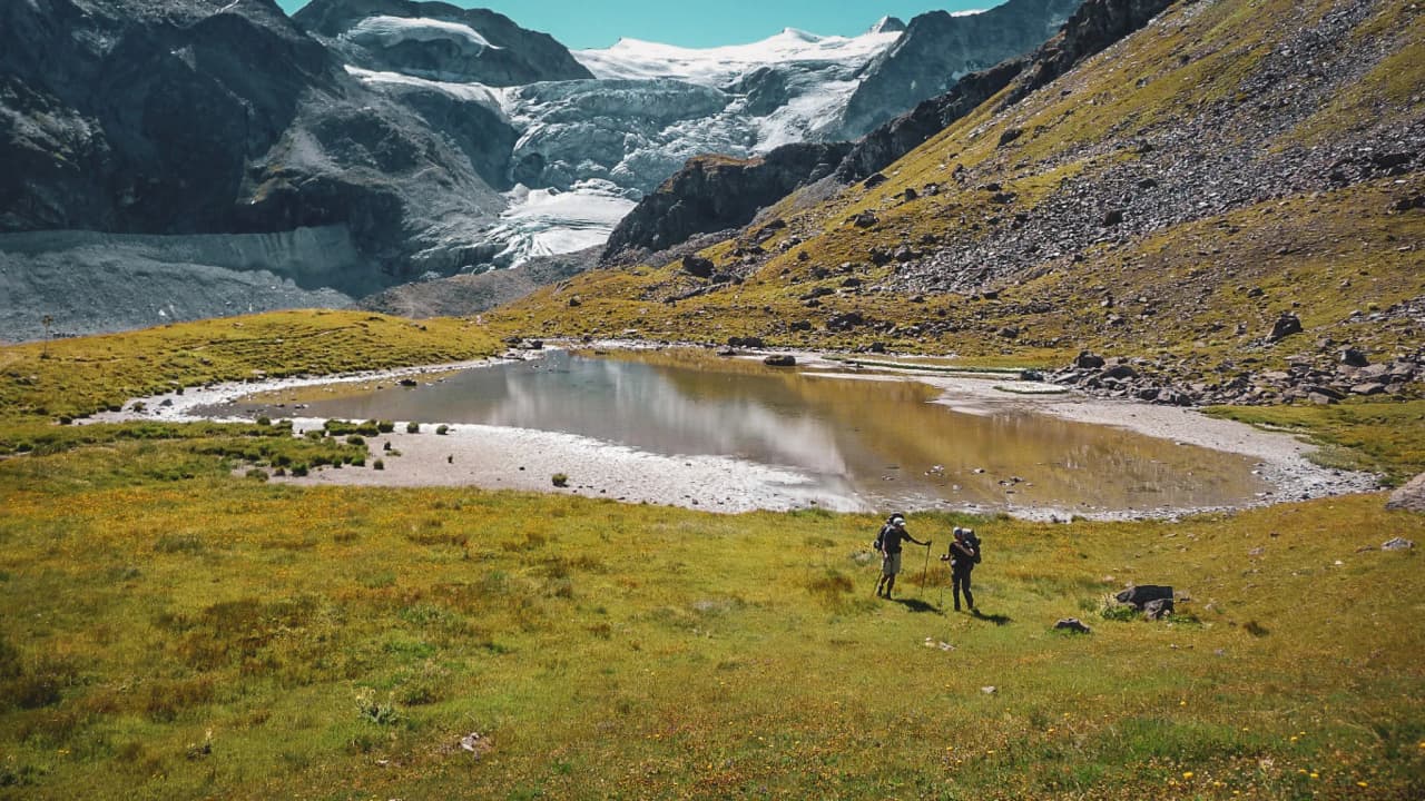Randonneurs au bord d'un lac, avec le majestueux Glacier d'Aletsch en arrière-plan.