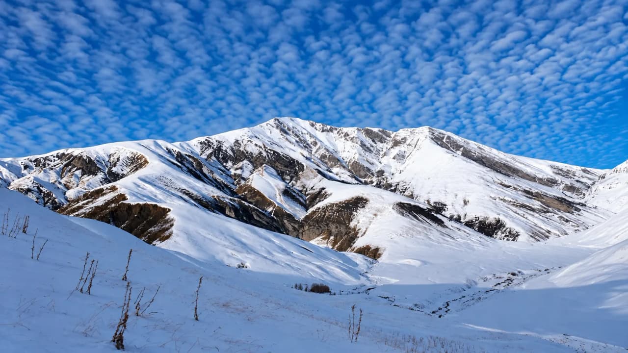 A snow-covered mountain landscape with a majestic peak and a blue sky dotted with clouds.