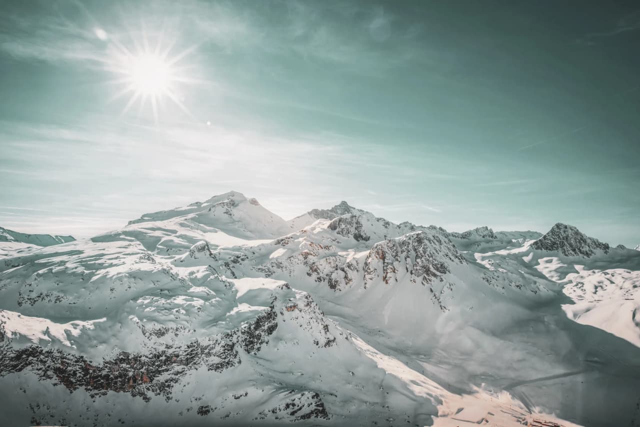 Een besneeuwd en zonnig landschap, met majestueuze bergen onder een stralend blauwe hemel.