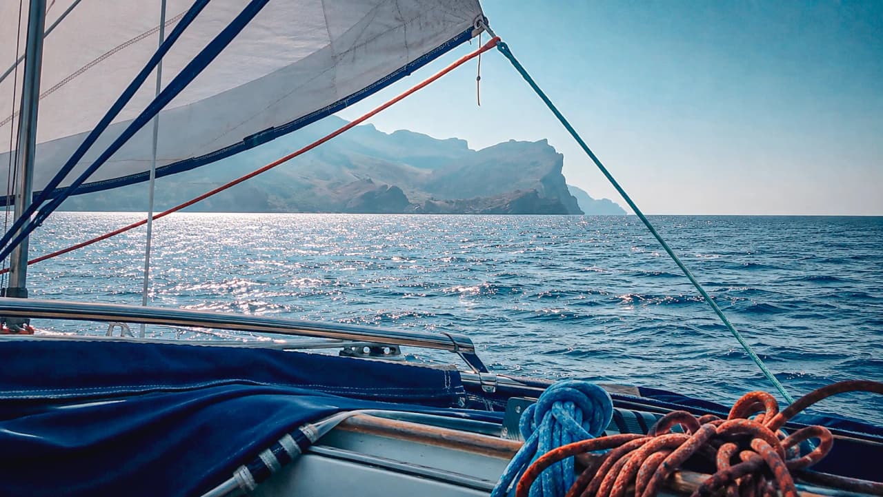 A sun-drenched view from a sailing boat, with the coves of the Balearic Islands in the background.