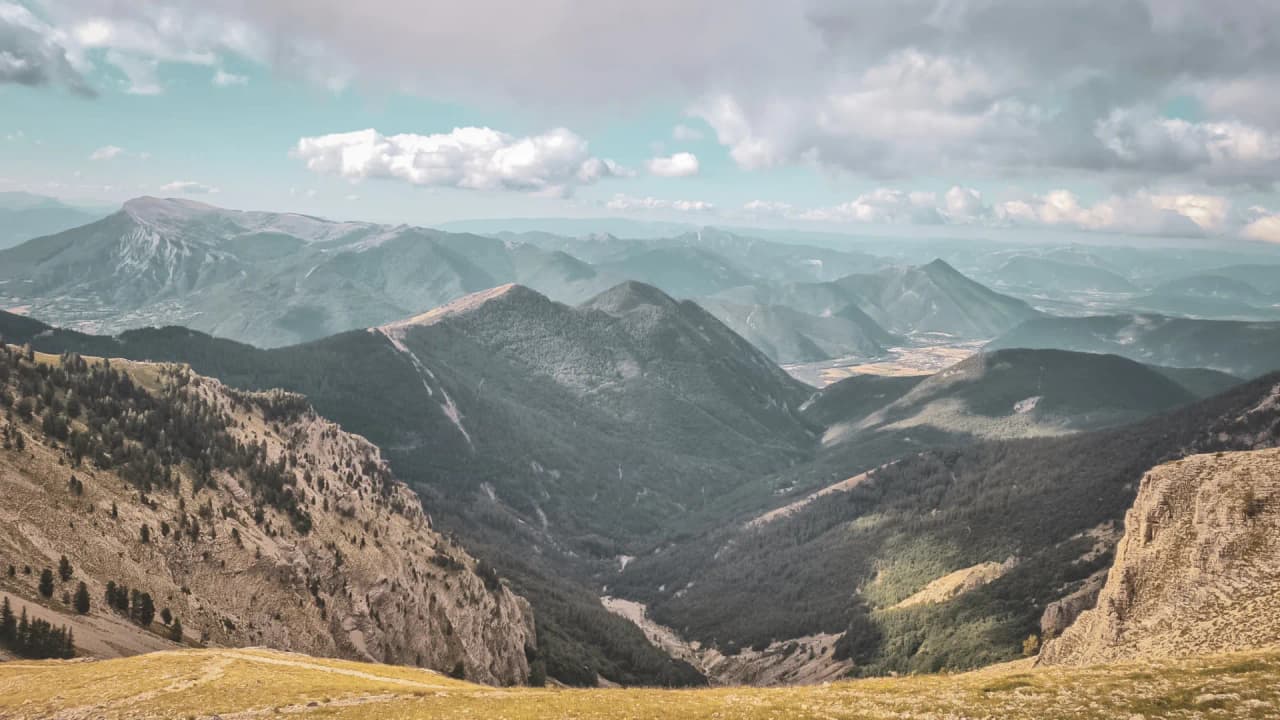 The mountainous landscape of Dévoluy, wild ridges and green valleys under a cloudy sky.