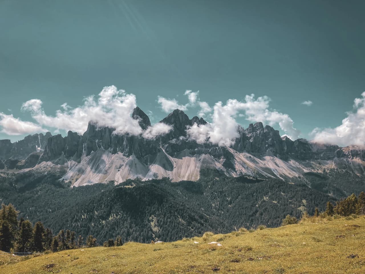 Majestic mountains, topped by light clouds, rise up against a clear sky. Lush green vegetation covers the foreground, adding a touch of lush nature to the landscape.