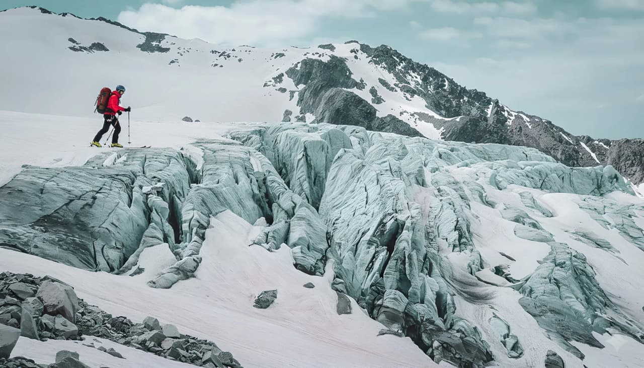 Un skieur solitaire traverse un glacier épuré, entouré de montagnes majestueuses.