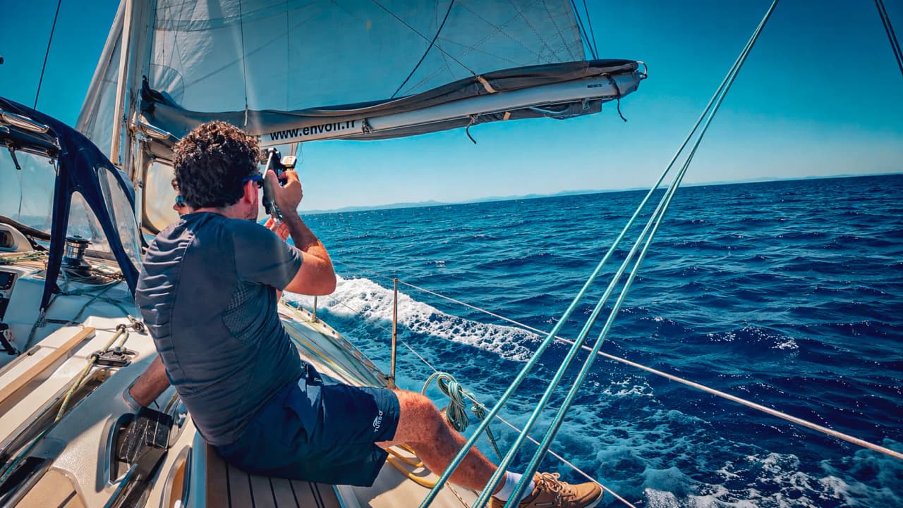 Sailing aboard a yacht, a man takes photographs of the azure waters of the Balearic Islands.