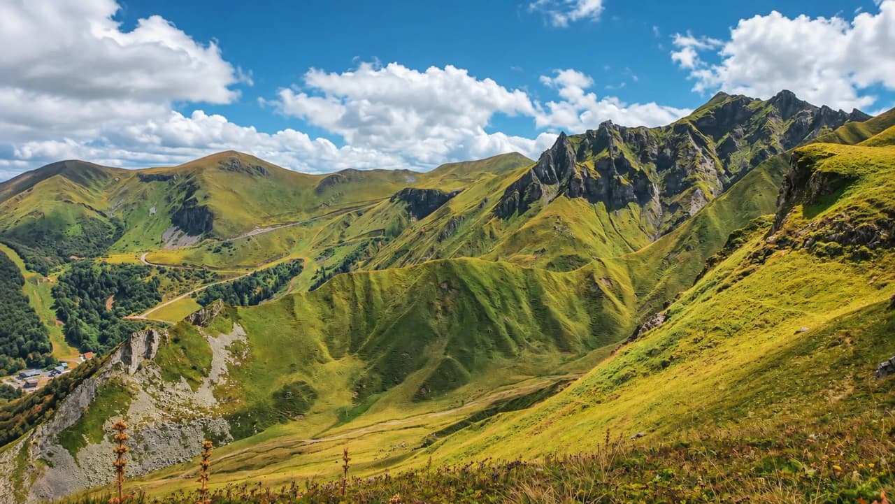Vue panoramique des collines verdoyantes du Massif Central sous un ciel bleu ponctué de nuages.
