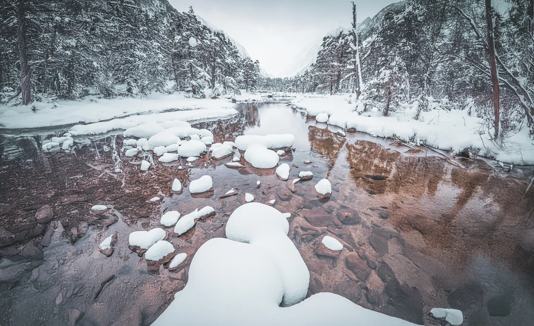 A peaceful river surrounded by mountains in winter, covered in snow and enchanting reflections.