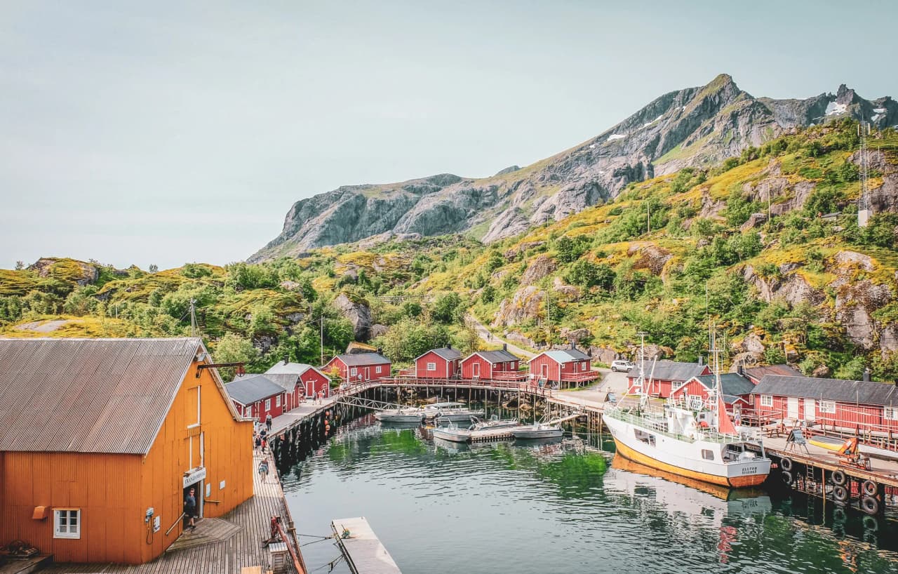A picturesque view of the Lofoten Islands, with red huts and green mountains, ideal for adventure.