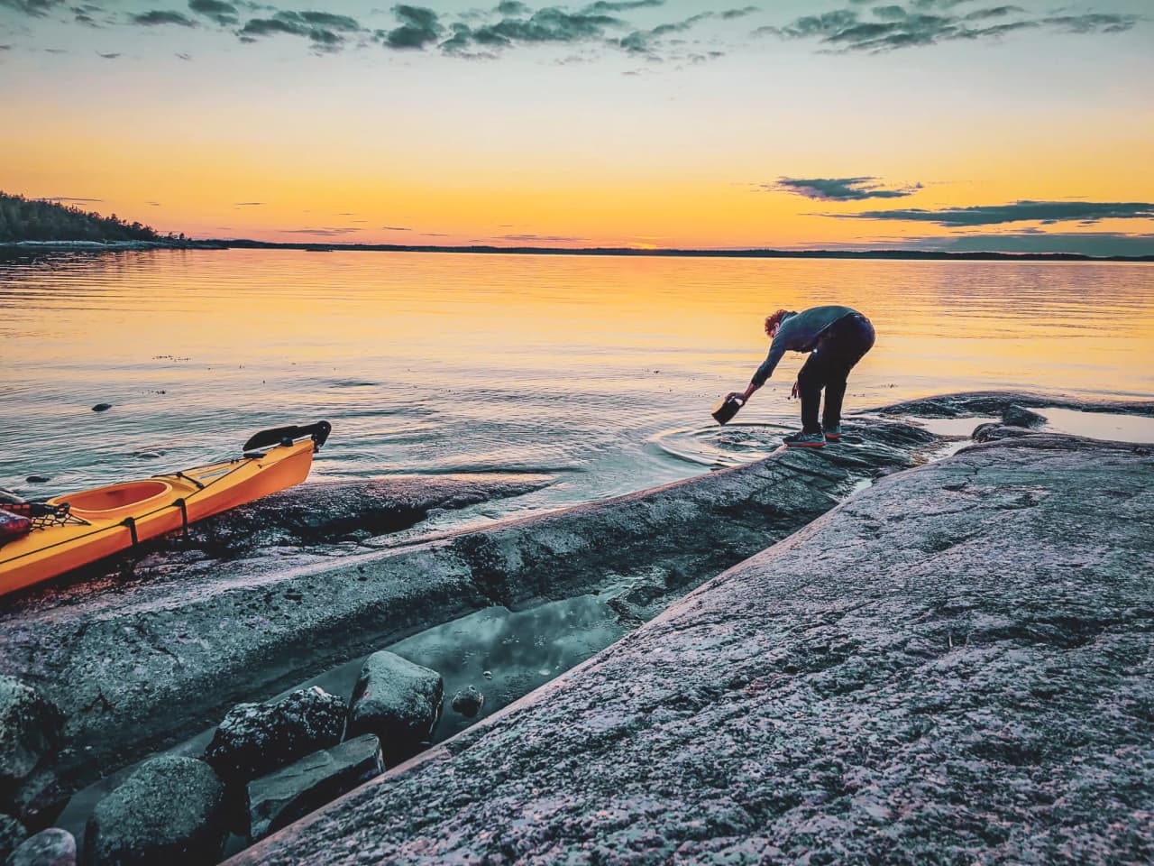 A yellow kayak at the edge of calm water, an adventurer captures the sunset over the Stockholm archipelago.