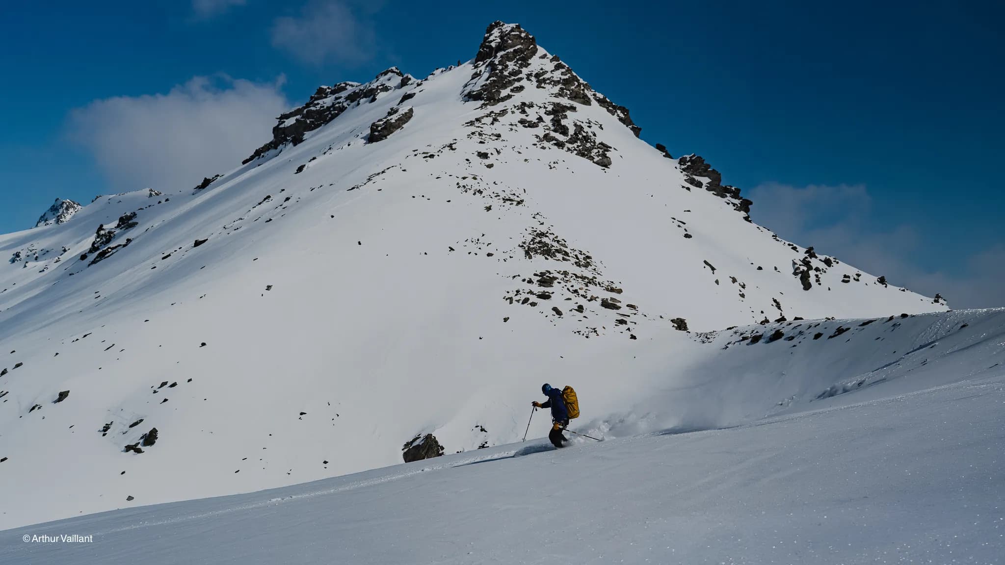 A skier making their way down a snow-covered Alpine slope, with majestic peaks in the background.