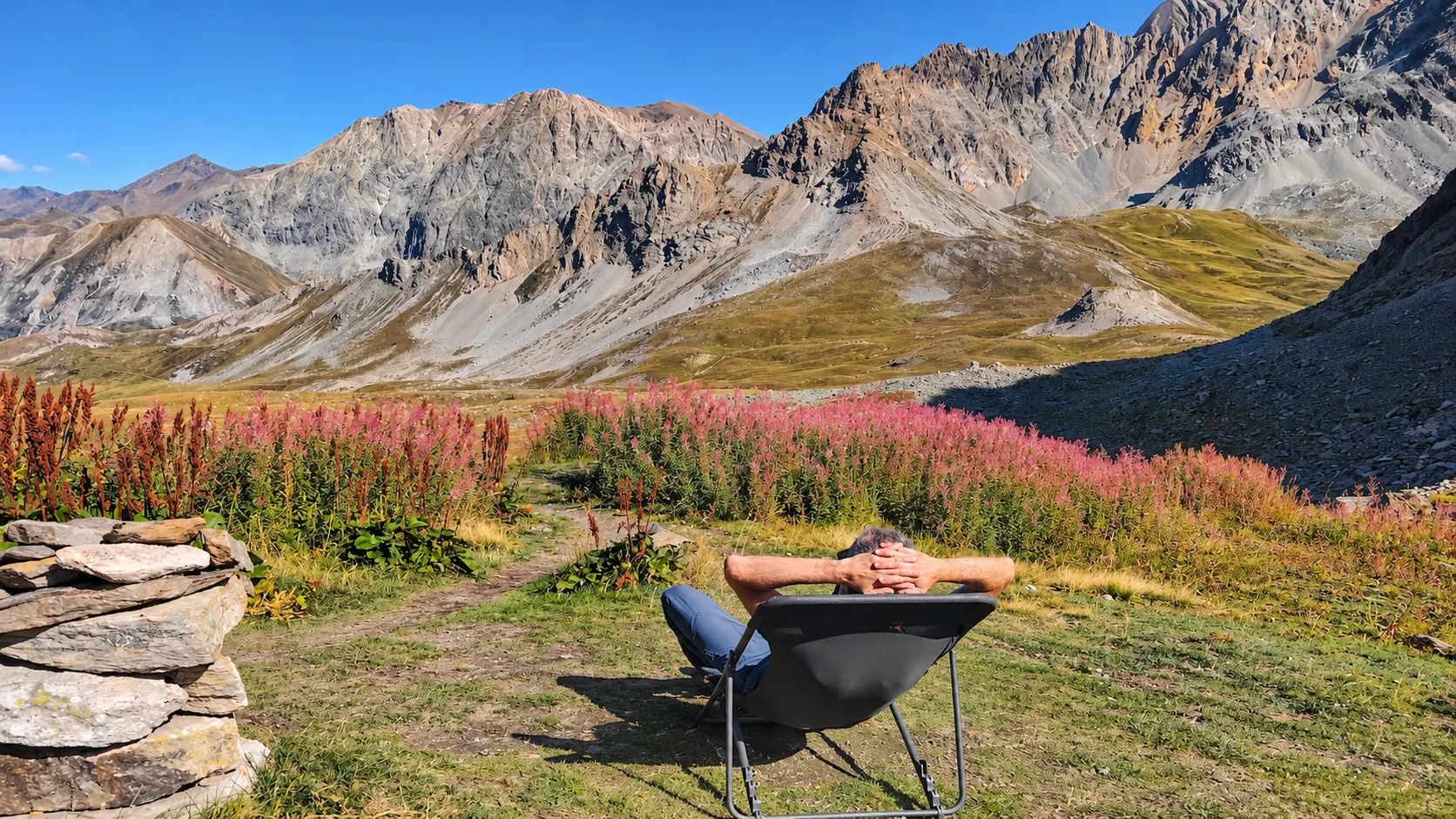 A man relaxing in an armchair, surrounded by flowers and majestic mountains.