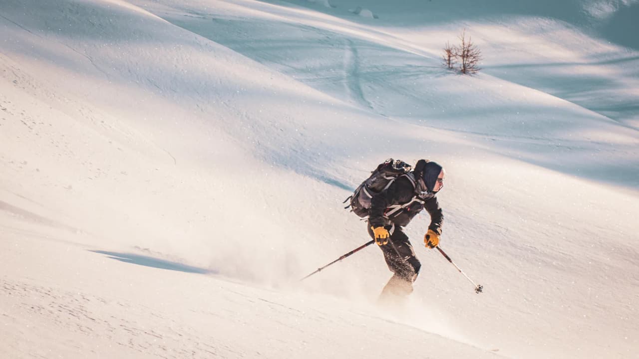 Un skieur glisse sur des pentes enneigées du Queyras, sous un ciel éclatant, invitant à l'aventure.